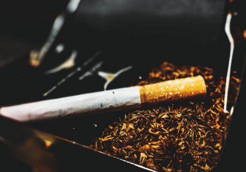 Cigarrillo hecho a mano sobre una superficie con tabaco suelto, resaltando la textura del tabaco y el diseño del cigarrillo.