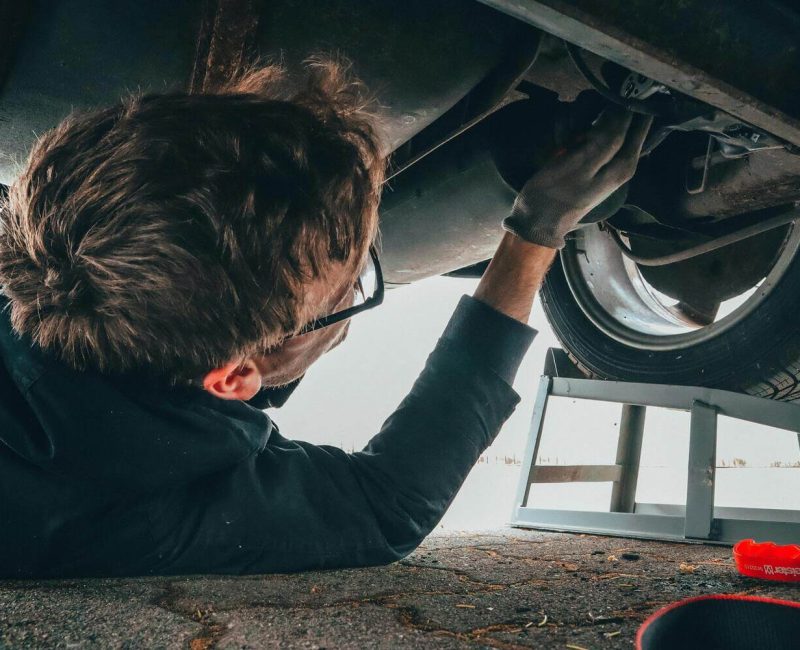 Técnico realizando mantenimiento en el sistema de suspensión de un vehículo, trabajando bajo el automóvil con herramientas en mano.
